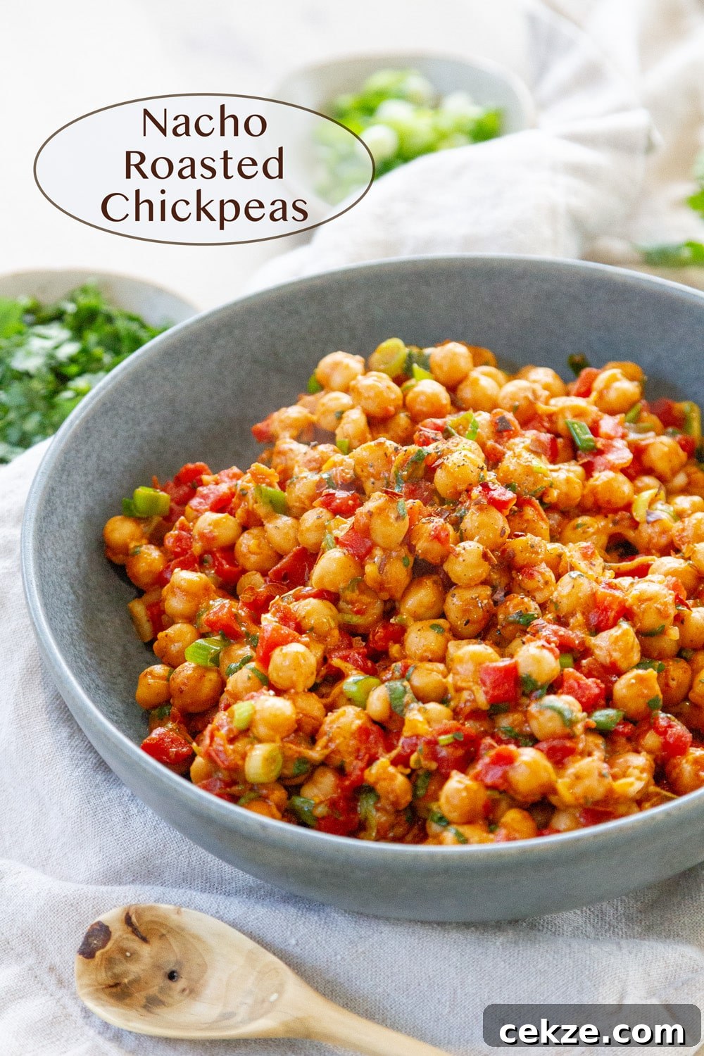 a large bowl filled with nacho roasted chickpeas a wooden spoon in the lower left and small bowls of cilantro and green onions for garnish.