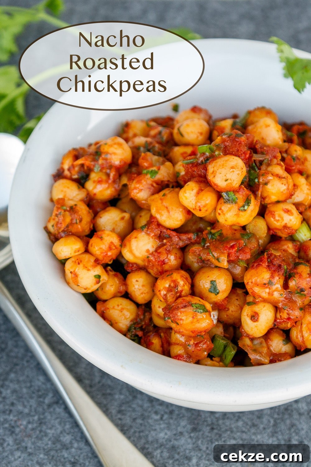 a white bowl filed with spiced garbanzo beans and a spoon to the left and cilantro around the bowl.