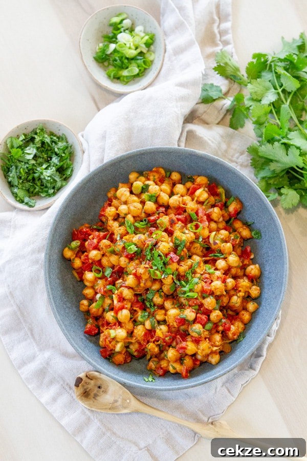 A large bowl filled with cooked chickpeas a wooden spoon below the bowl two smaller bowls with chopped fresh herbs and some cilantro on the upper right.