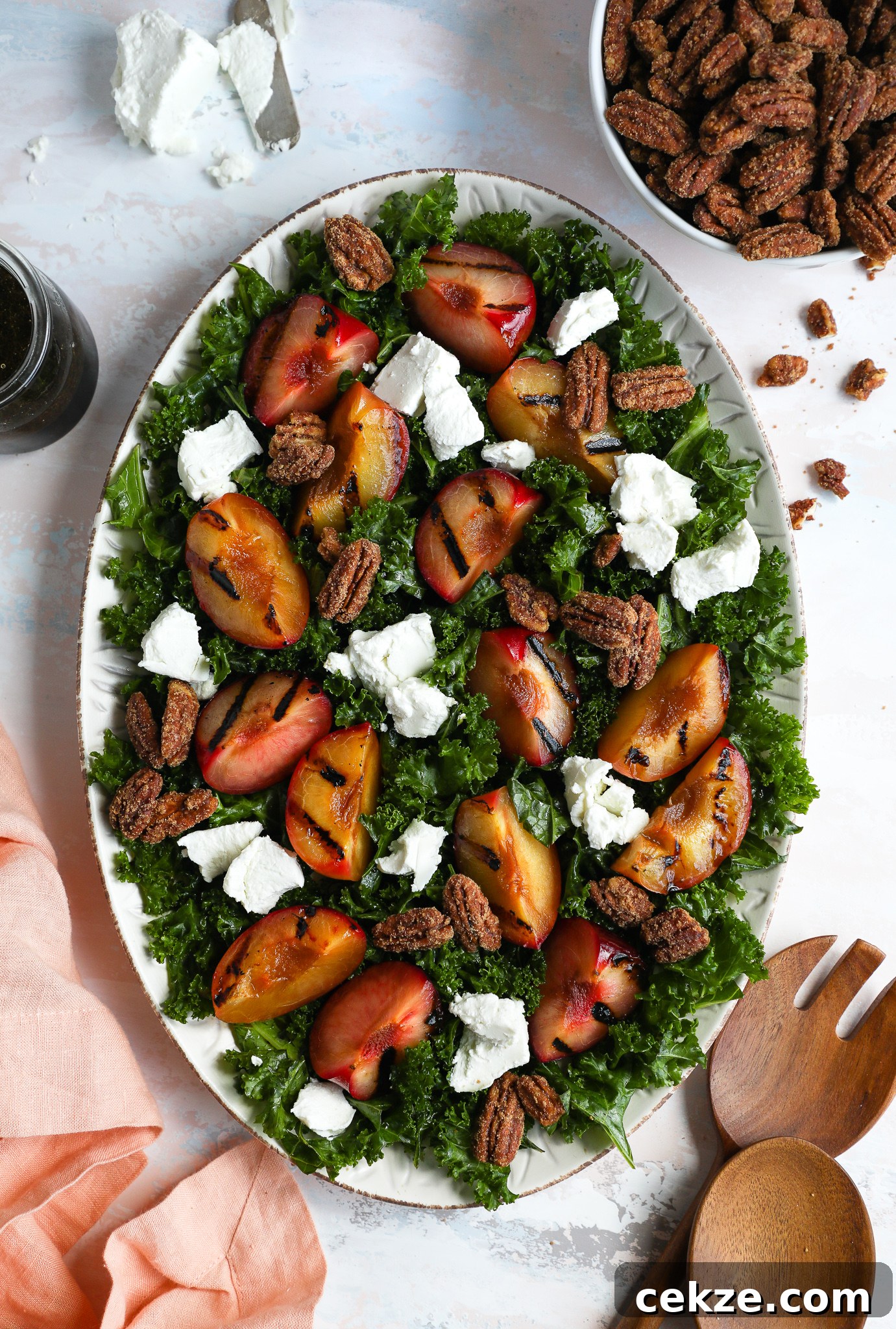 A large serving tray filled with a salad made with massaged kale, goat cheese, candied pecans and plumcots