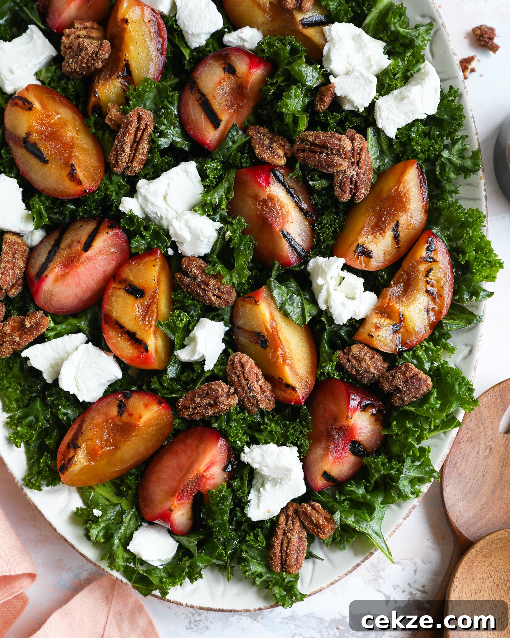 Grilled plumcot kale salad served on a large oval tray topped with candied pecans