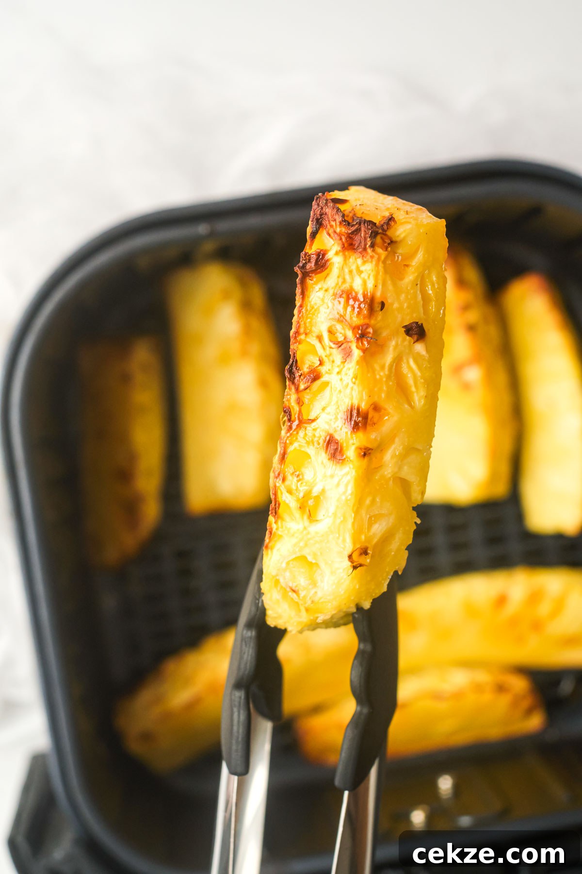 one piece of air fryer pineapple held with tongs