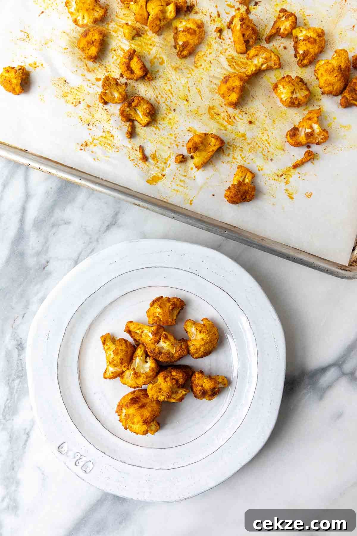 Crispy Spicy Roasted Cauliflower with Chili and Garlic 8 Florets of spicy roasted cauliflower on a white plate and on a baking sheet beside it.