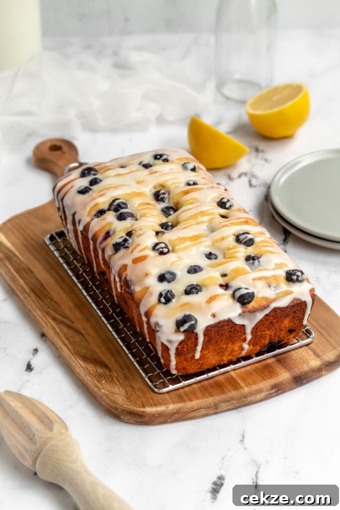 A lemon ricotta pound cake topped with lots of blueberries and icing on a rack.