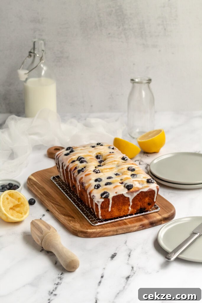 Blueberry loaf dripping with icing on a wire rack and plates nearby.