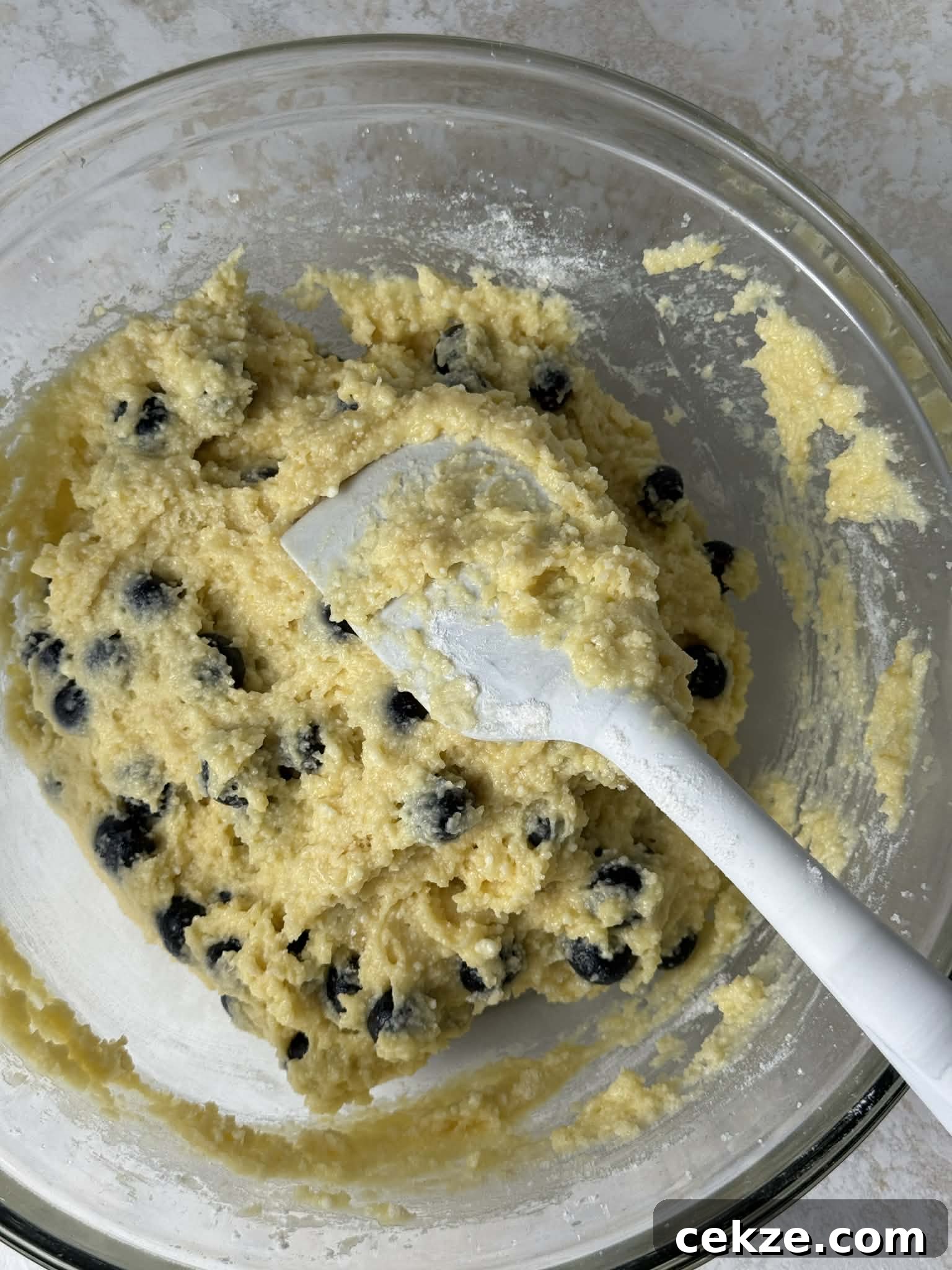 Folding blueberries into cake batter with a spatula.