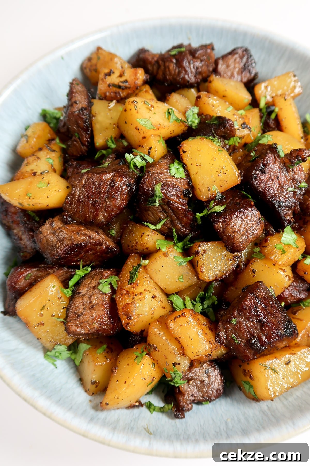 Garlic Butter Steak and Potatoes Skillet Recipe for Weeknights 8 Cooked steak bites and potatoes on a plate for serving. Fresh parsley is sprinkled on top.