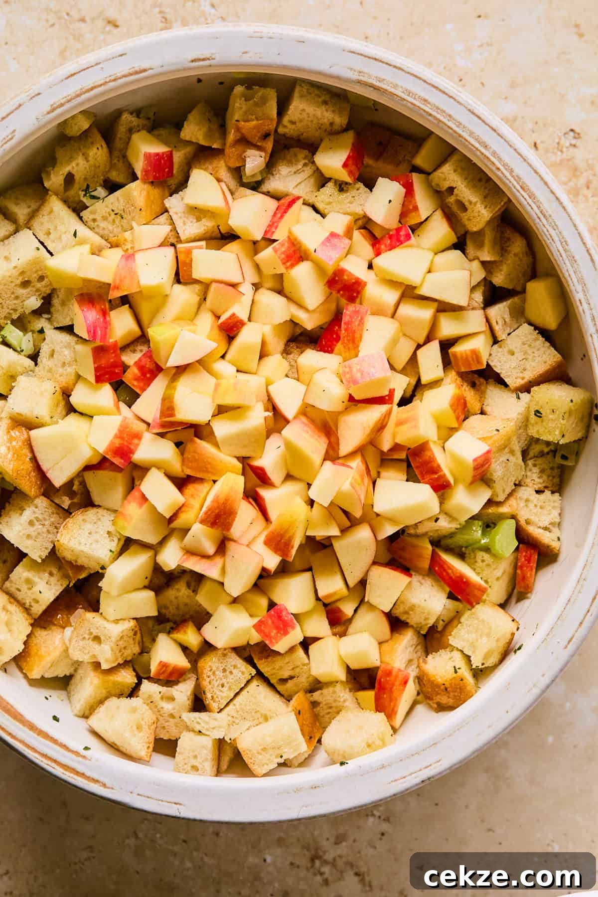 Apple and Sage Stuffing Recipe with Crispy Herbs 7 Celery and onion mixture added to mixing bowl with chopped apples added on top.