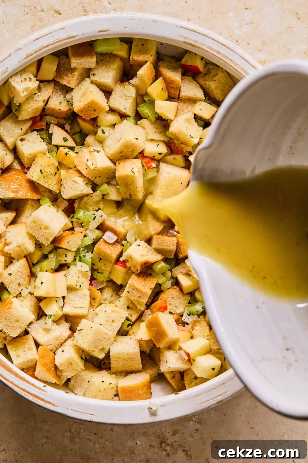 Apple and Sage Stuffing Recipe with Crispy Herbs 9 Broth mixture added to bowl with apple stuffing ingredients.