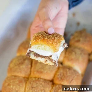 A hand holding a smores pull-apart bread piece with chocolate and melted marshmallow. The bread is golden brown with a crumb topping. In the background, the rest of the smores pull-apart is visible.