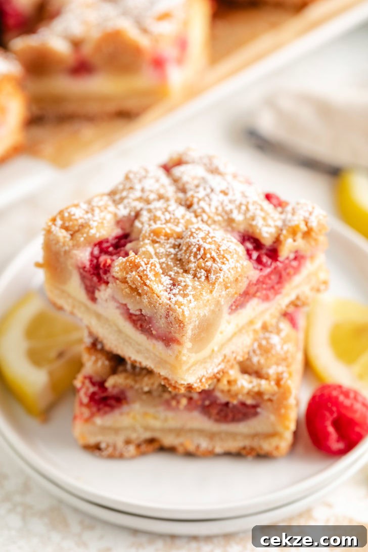 Lemon raspberry crumb bars stack on white plates and sprinkled with powdered sugar.