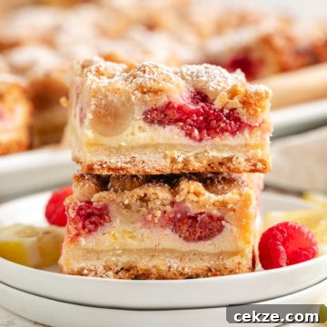 Close up view of a stack of lemon raspberry crumb bars next to fresh berries on plates.