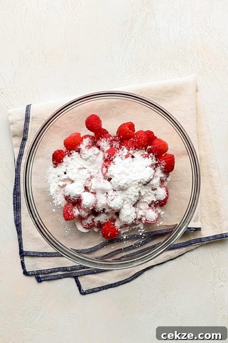 Fresh raspberries, granulated sugar, and cornstarch in a glass mixing bowl.