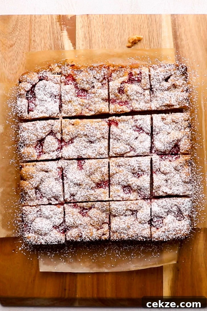 Sliced lemon raspberry bars on a cutting board dusted with powdered sugar.