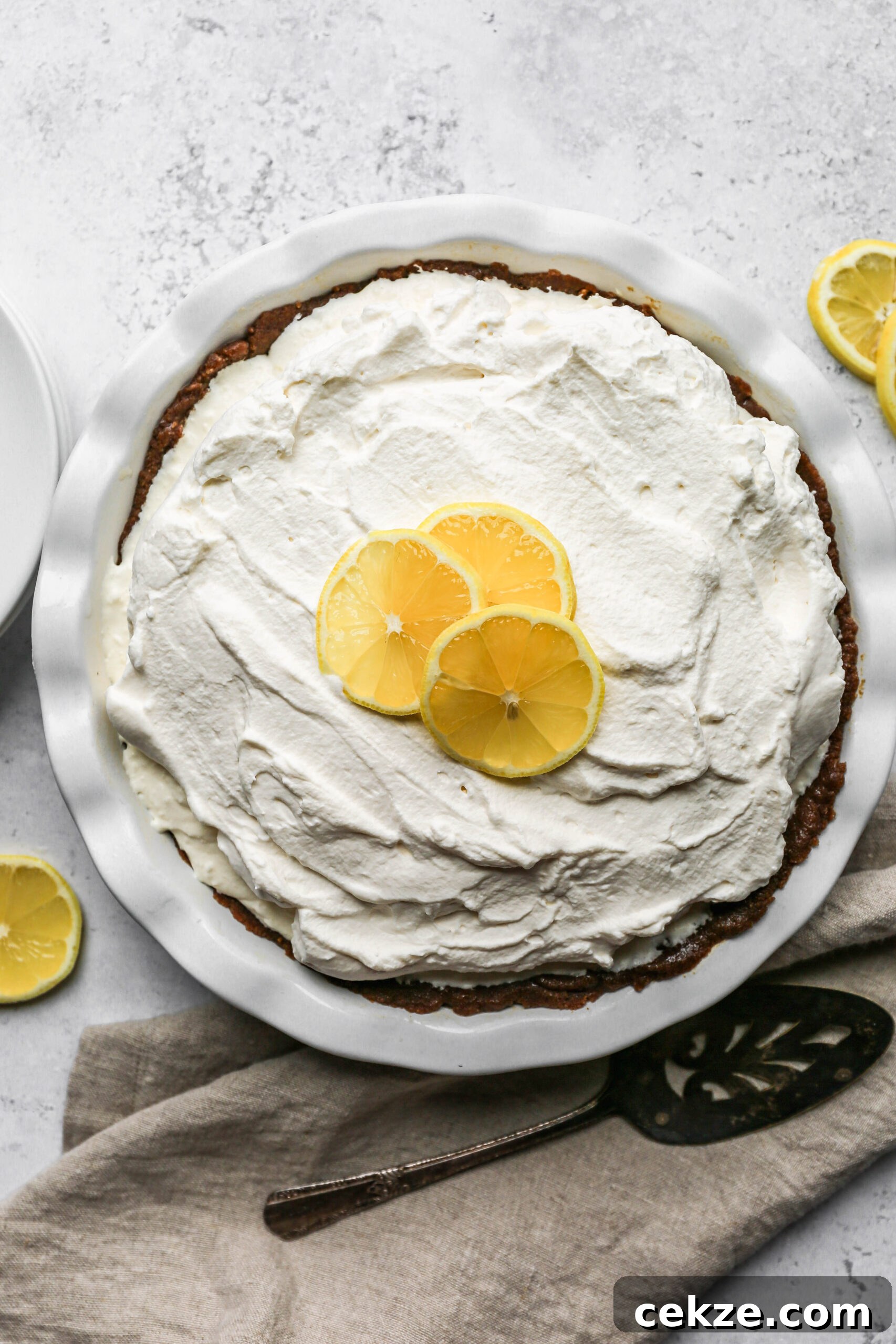 Gluten-Free No-Bake Lemon Icebox Pie Recipe 2 a white pie plate of gluten free no bake lemon icebox pie next to lemon slices.
