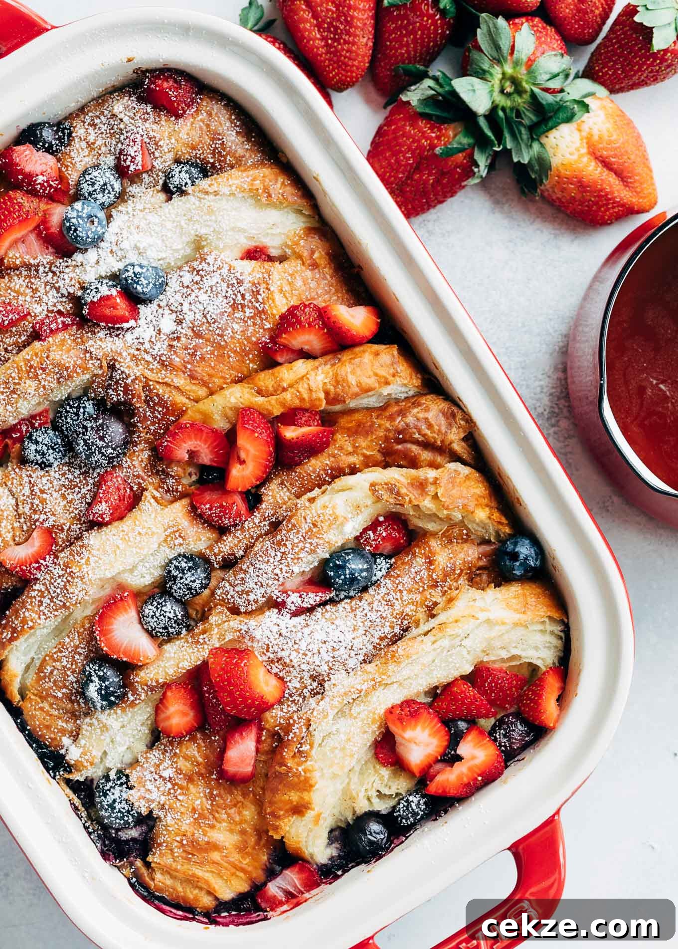 overnight croissant baked french toast with strawberries and blueberries in a stub casserole dish