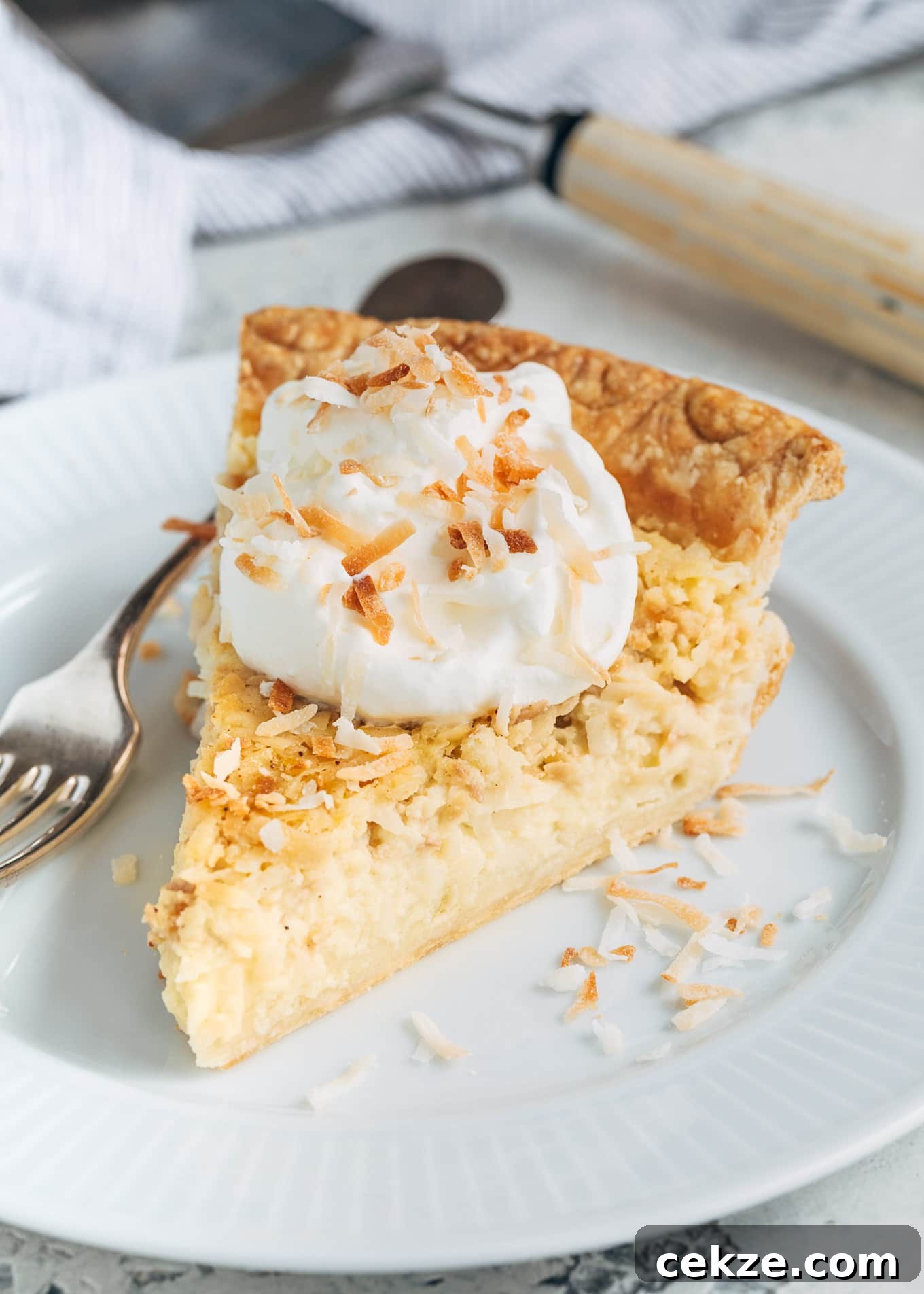 slice of coconut custard pie on a plate with whipped cream and toasted coconut flakes