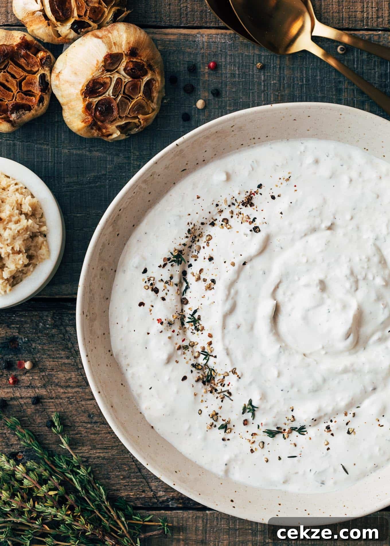 horseradish cream sauce in an ivory bowl on a wood board with roasted garlic heads and a bowl of horseradish on the side