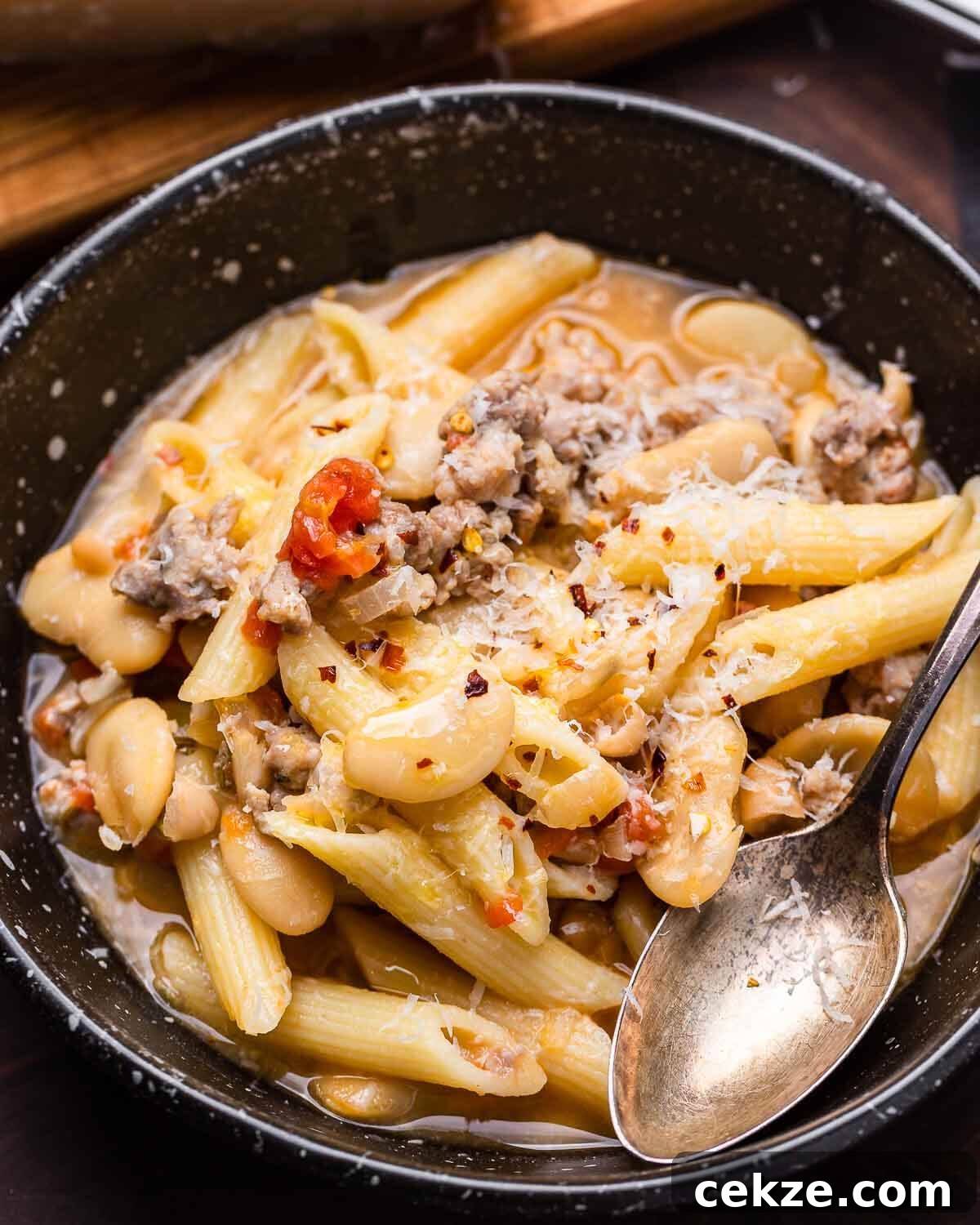 Black bowl of sausage pasta fagioli with grated cheese and spoon.