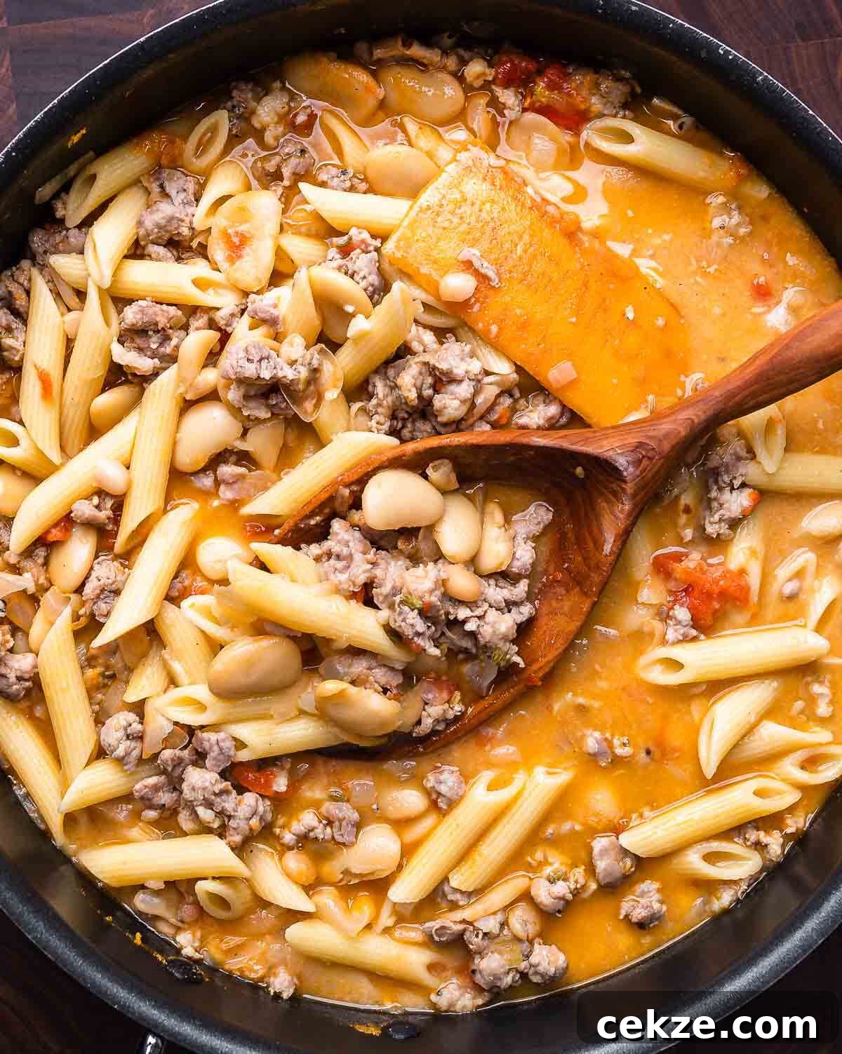 Overhead shot of sausage pasta fagioli in black pot with wooden spoon.