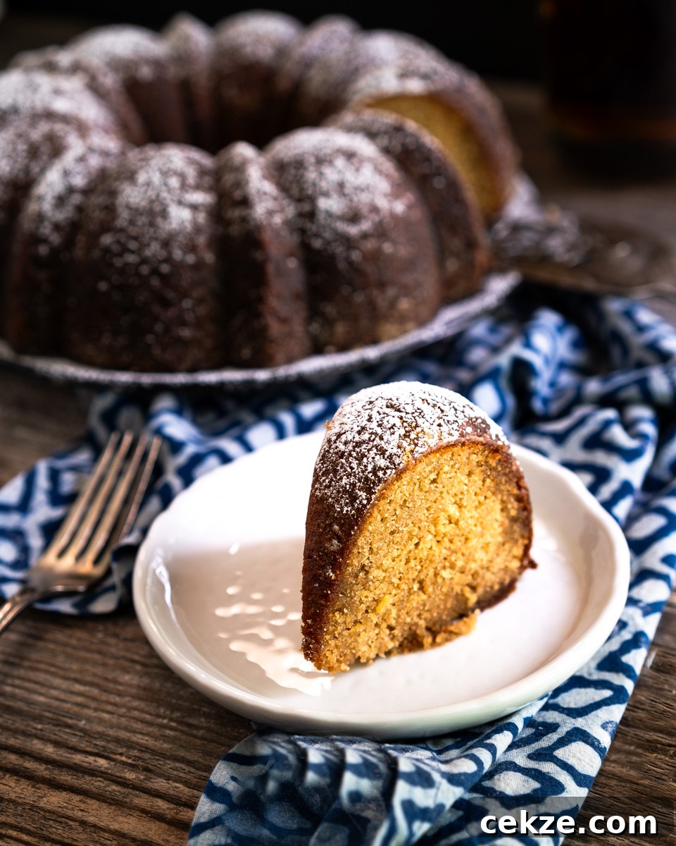 Authentic Cuban Rum Cake Recipe: Moist Drunken Cake with Rum Glaze 11 Sideview of a slice of Drunken Rum Cake sitting on a plate in front of the bundt cake. Hostess At Heart