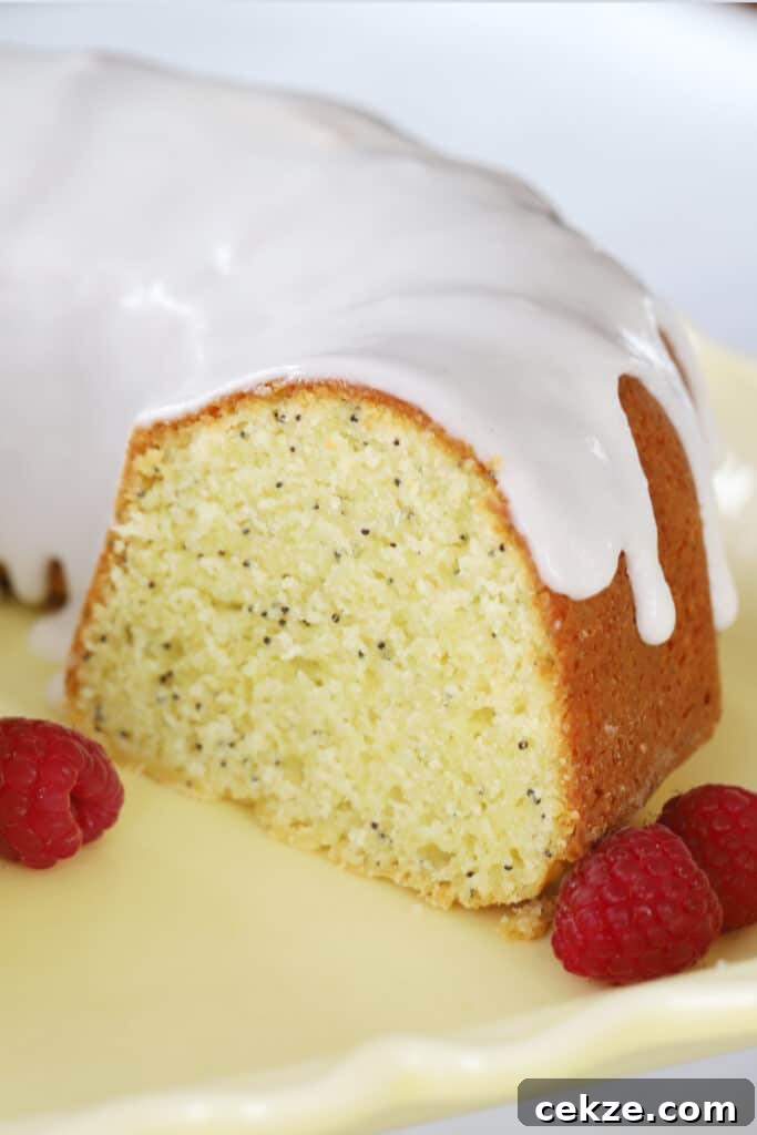 A lemon poppy seed bundt cake on a plate, covered with glaze and sliced to show the inside.