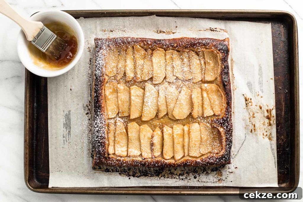 Rustic Apple Tart Recipe: Flaky Crust and Caramelized Apples 3 apple tart on a baking sheet with apricot jam in a bowl.
