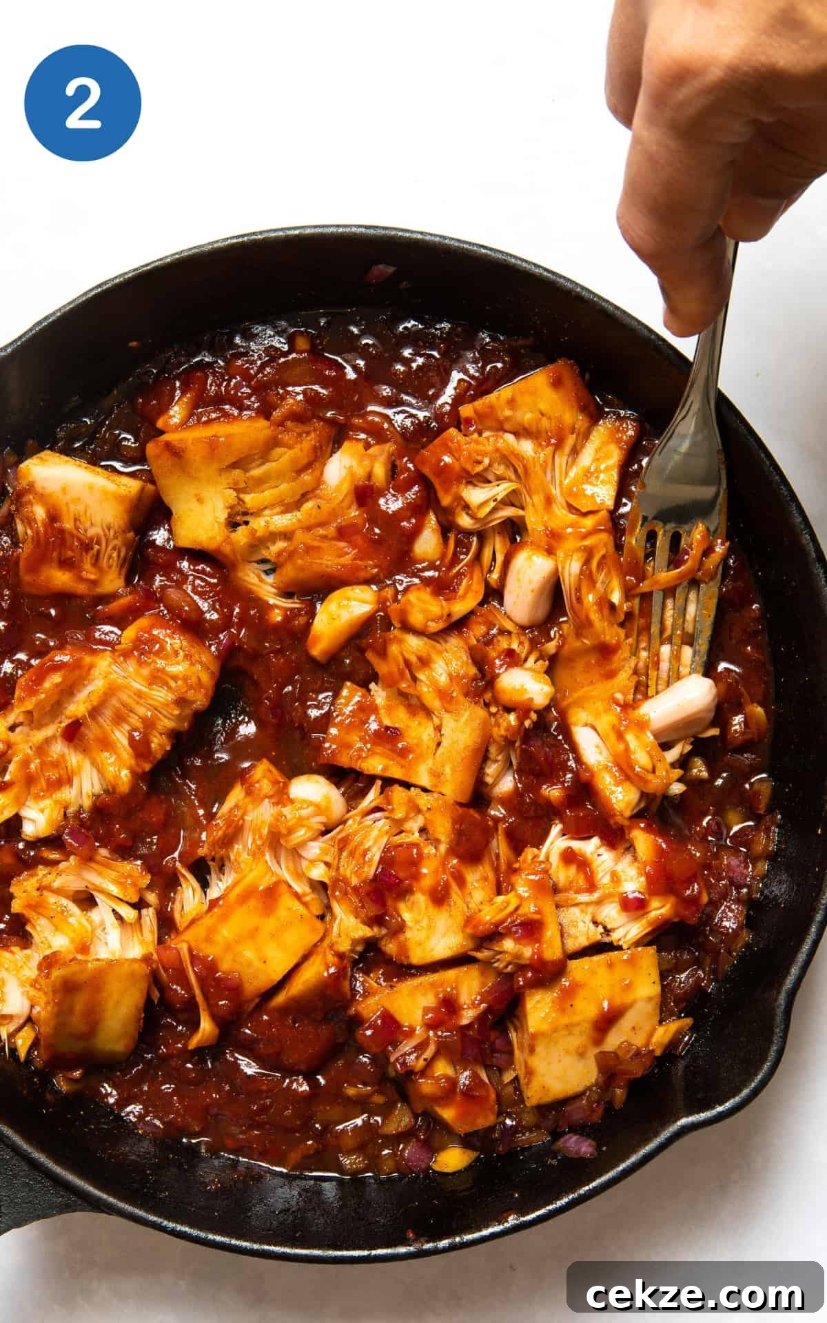 hand pressing jackfruit in a pan with a sauce.