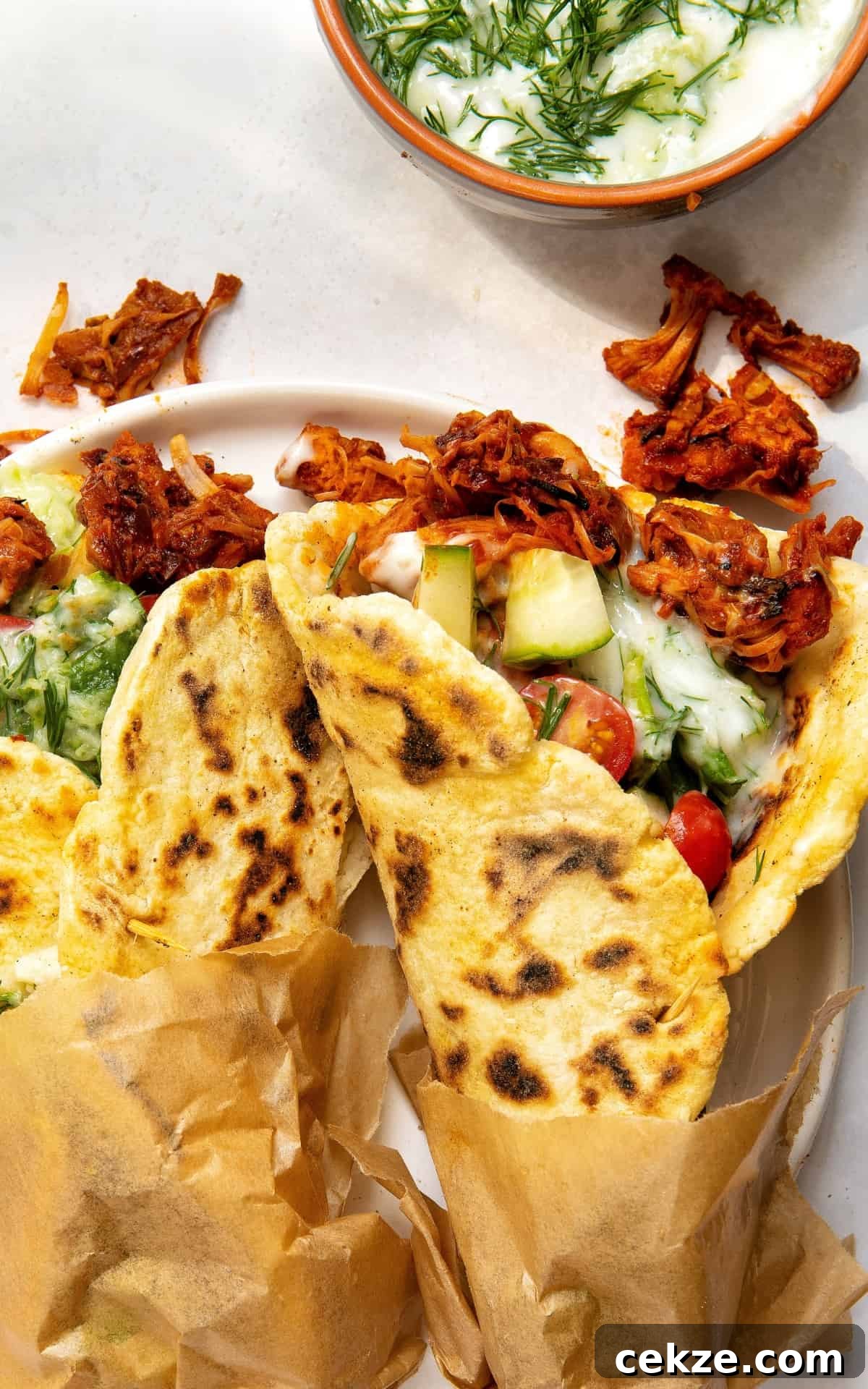 Two vegan gyros served on a plate with fresh vegetables and tzatziki.