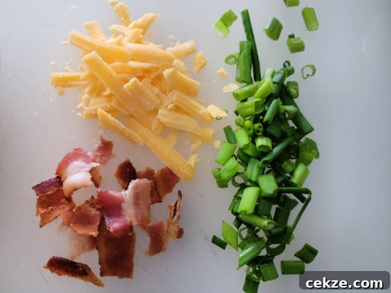 Creamy Bacon Cheddar Ranch Dip Recipe for Parties and Game Day 7 shredded cheddar cheese, bacon pieces, and chopped green onion on a cutting board.