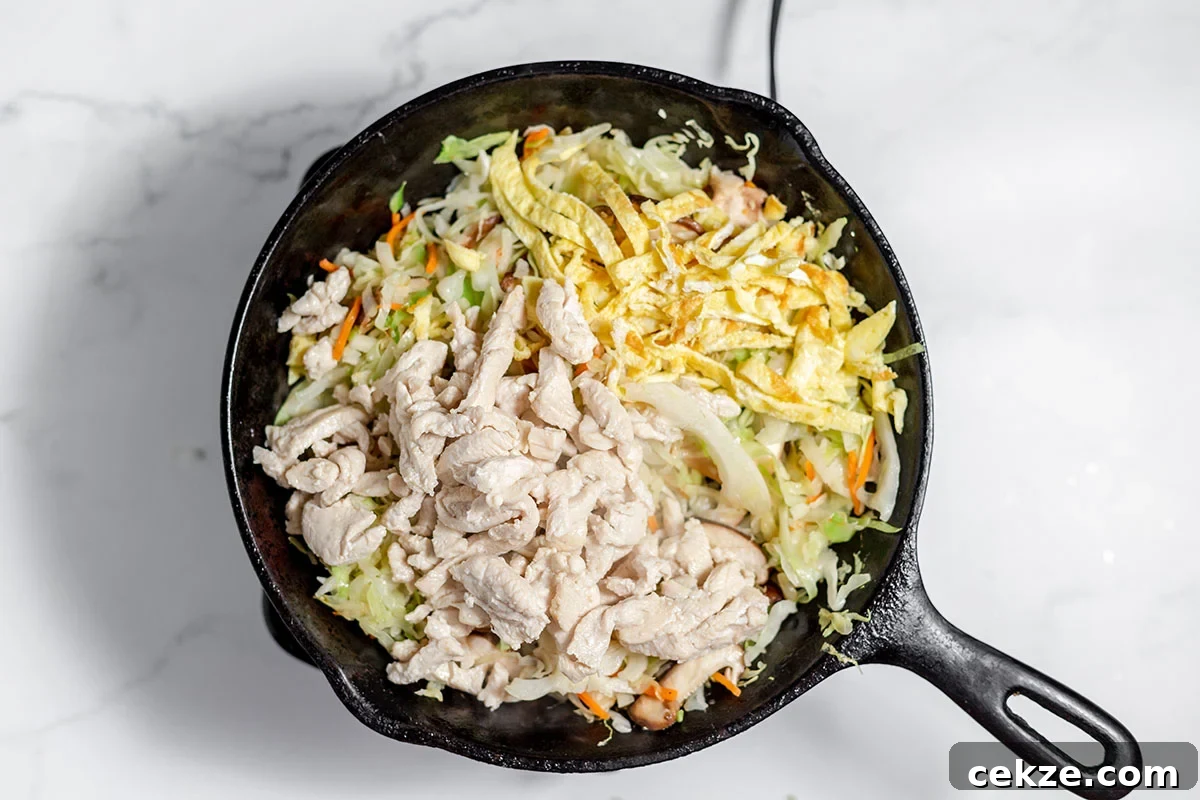Chicken and eggs are added to coleslaw mix and shiitake mushrooms in the cast iron skillet.