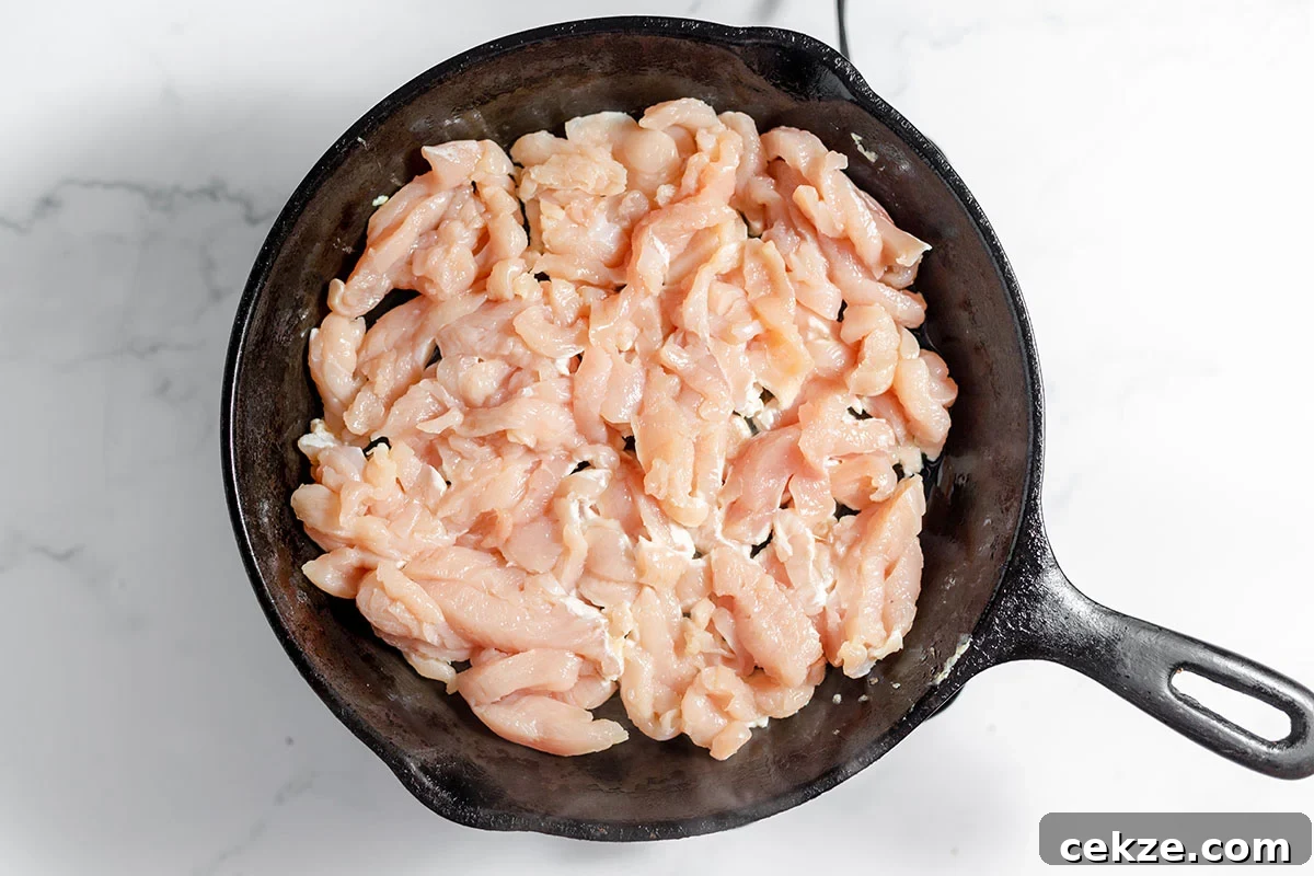 Uncooked chicken strips in a cast iron skillet.
