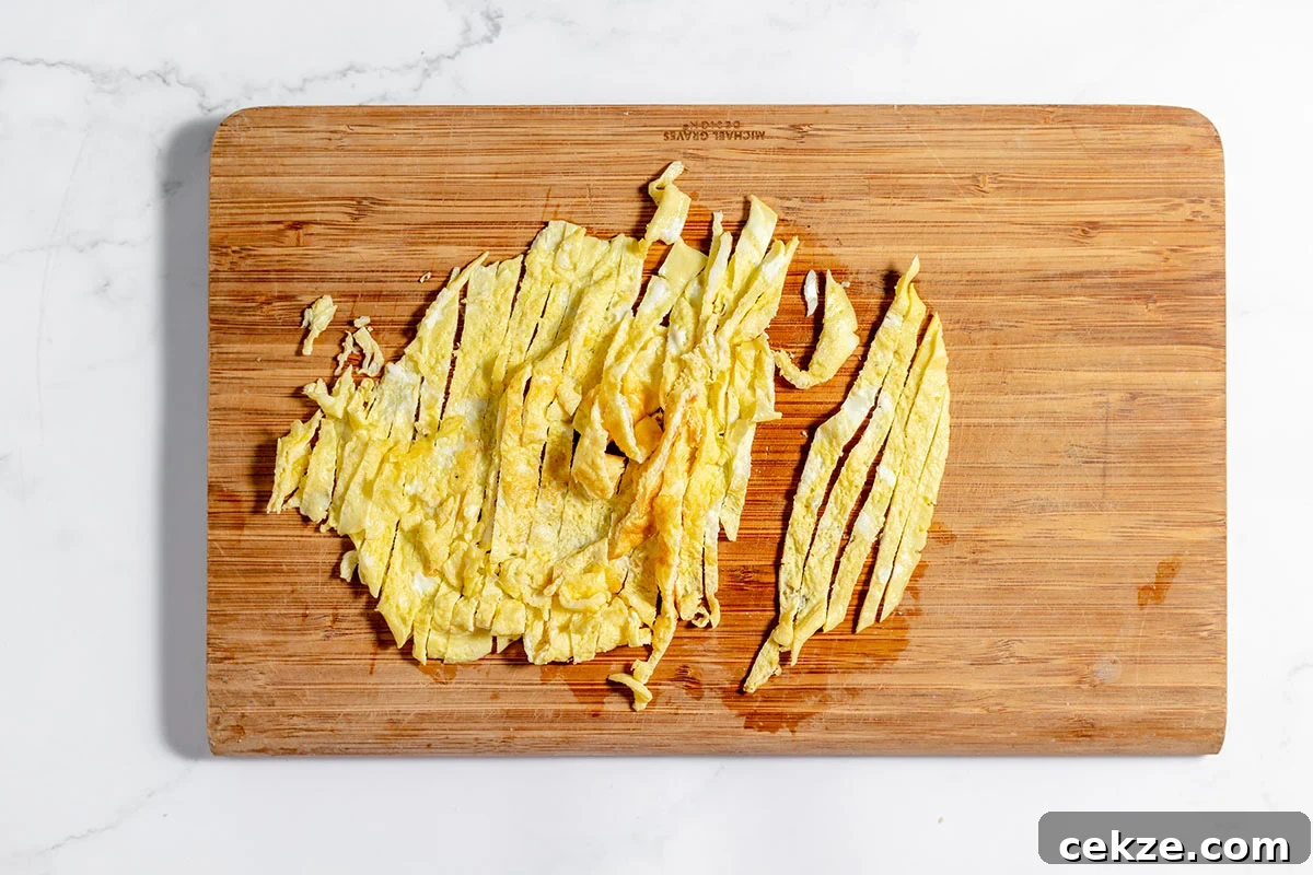 Eggs are cut into strips on a wooden cutting board.