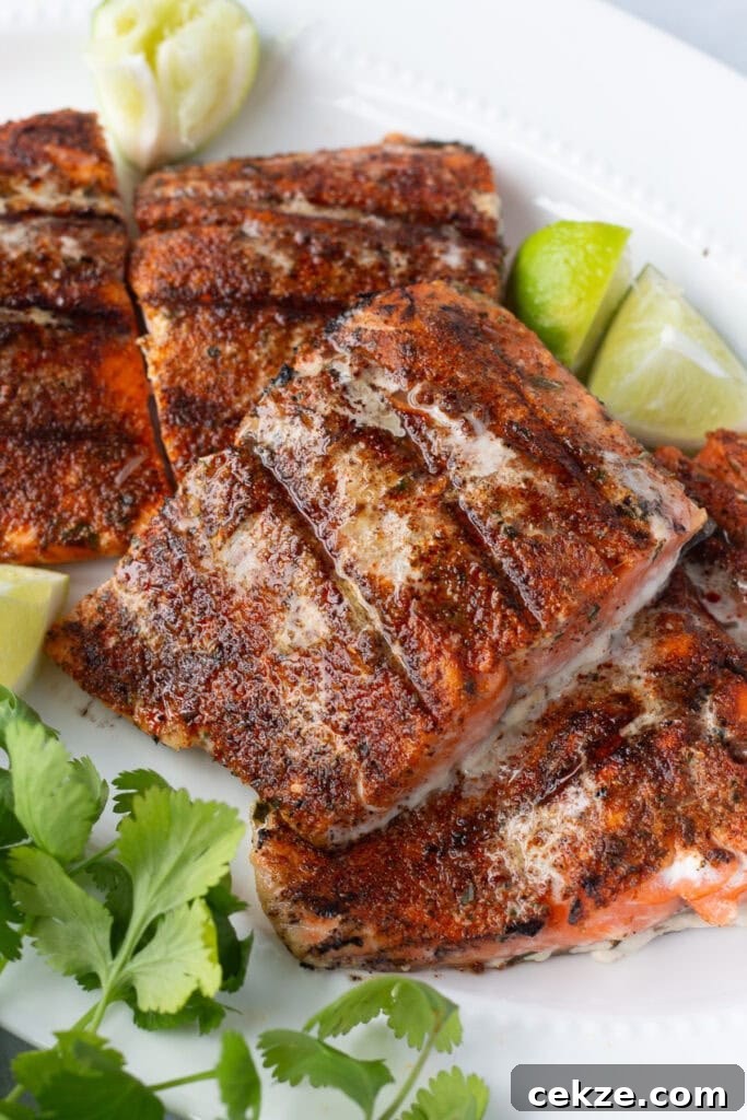 15-Minute Chili Lime Grilled Salmon Recipe 2 Close up of grilled chili lime salmon filets on a white platter with lime wedges and fresh herbs next to them.