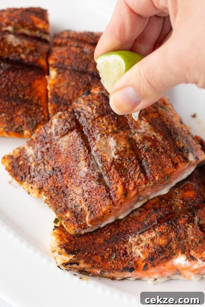 15-Minute Chili Lime Grilled Salmon Recipe 11 Close up of a hand squeezing a lime wedge over grilled salmon filets resting on a white platter.