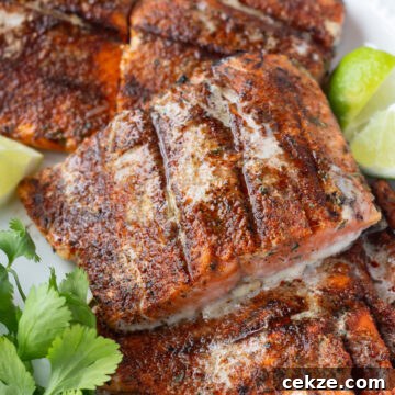 15-Minute Chili Lime Grilled Salmon Recipe 14 Close up of grilled chili lime salmon filets on a white platter with lime wedges and fresh herbs next to them.