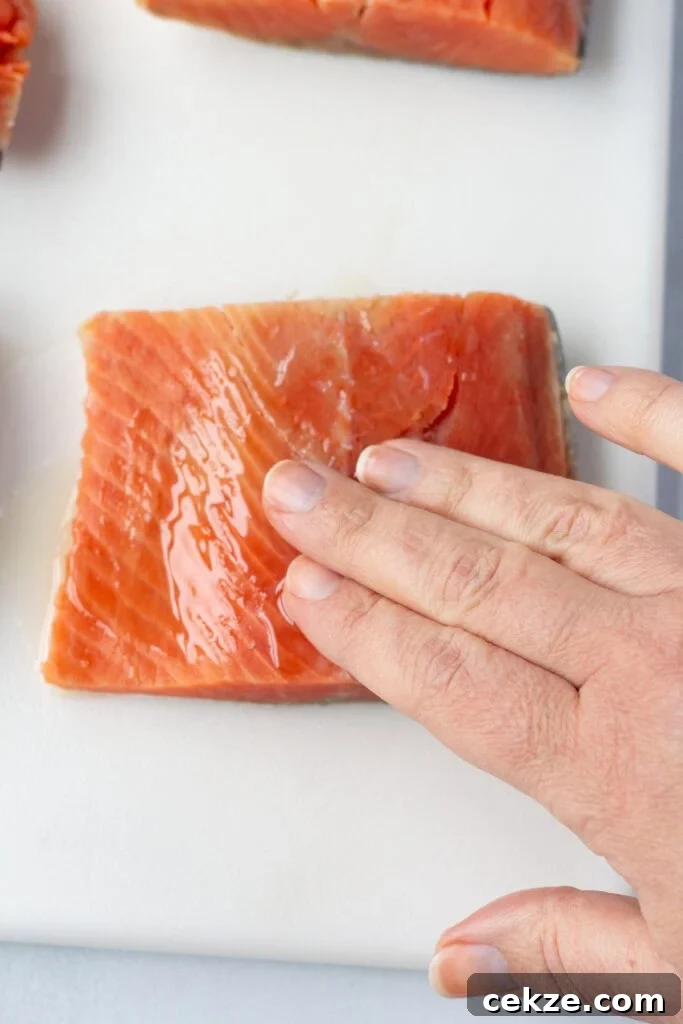 15-Minute Chili Lime Grilled Salmon Recipe 5 A hand rubbing oil onto a salmon filet on a white cutting board.