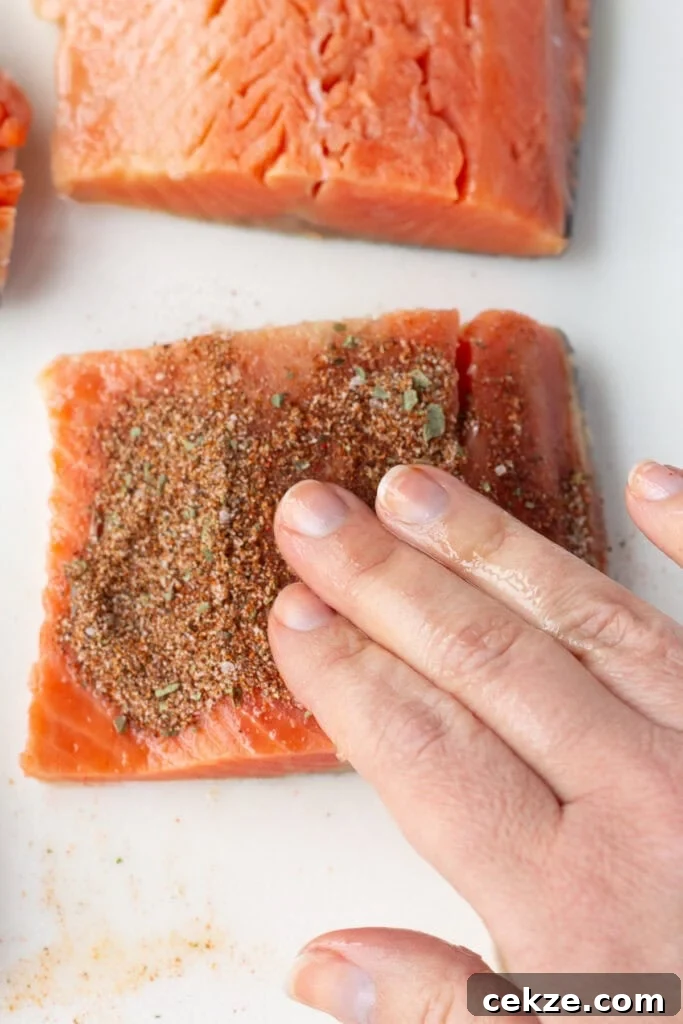 15-Minute Chili Lime Grilled Salmon Recipe 6 A hand rubbing a spice blend onto a salmon filet resting on a white cutting board.