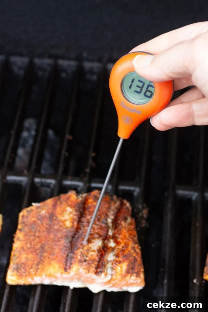 15-Minute Chili Lime Grilled Salmon Recipe 9 Picture of a meat thermometer with an bulbous orange head being put into a salmon filet on a grill with a temp reading of 136F.