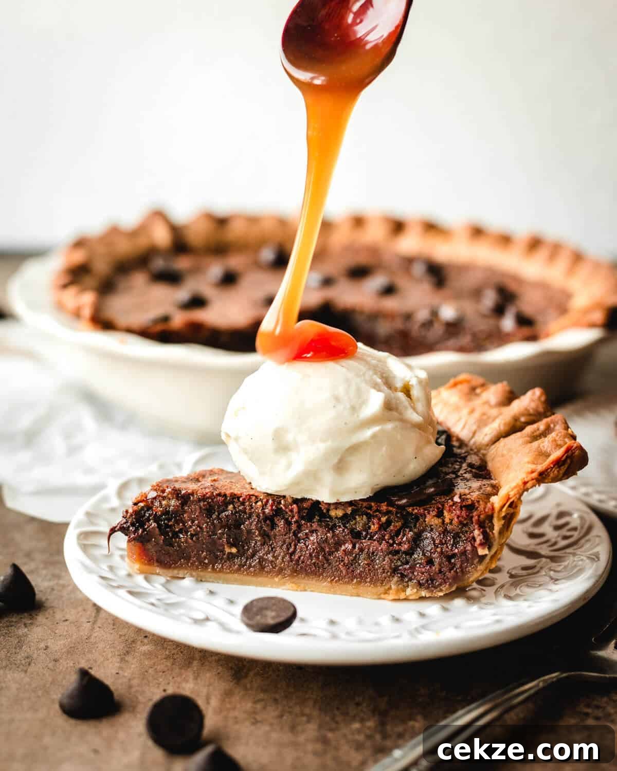 Ultimate Chocolate Chip Cookie Pie Recipe for Every Occasion 2 Wooden spoon with caramel drizzling over scoop of ice cream sitting on a slice of chocolate chip pie on a dessert plate.
