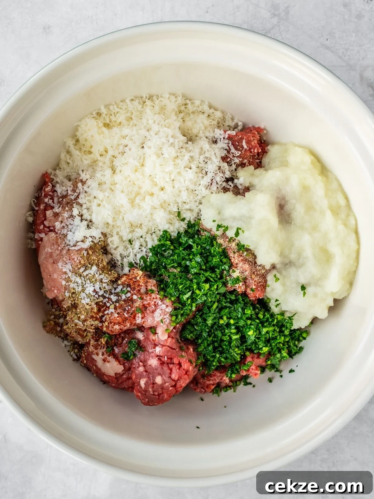 Juicy Italian Meatballs Without Breadcrumbs — Recipe & Tips 4 Bowl with ground meat, spices, parmesan cheese, grated onion and parsley.