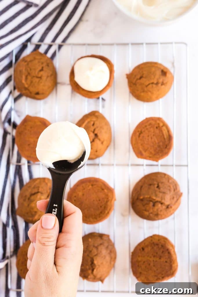 spooning cream cheese frosting over the pumpkin whoopie pie cookies