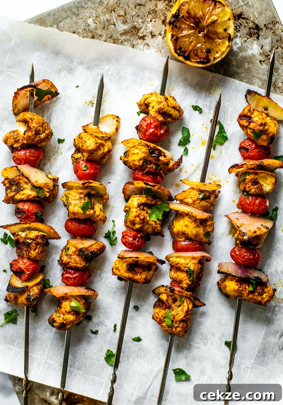 Grilled Moroccan chicken skewers set out over parchment paper with a grilled lemon half on the side.