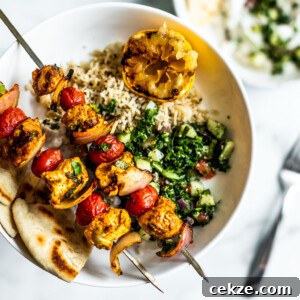 Plate of rice, tabbouleh, and pitas with grilled Moroccan chicken skewers on top.