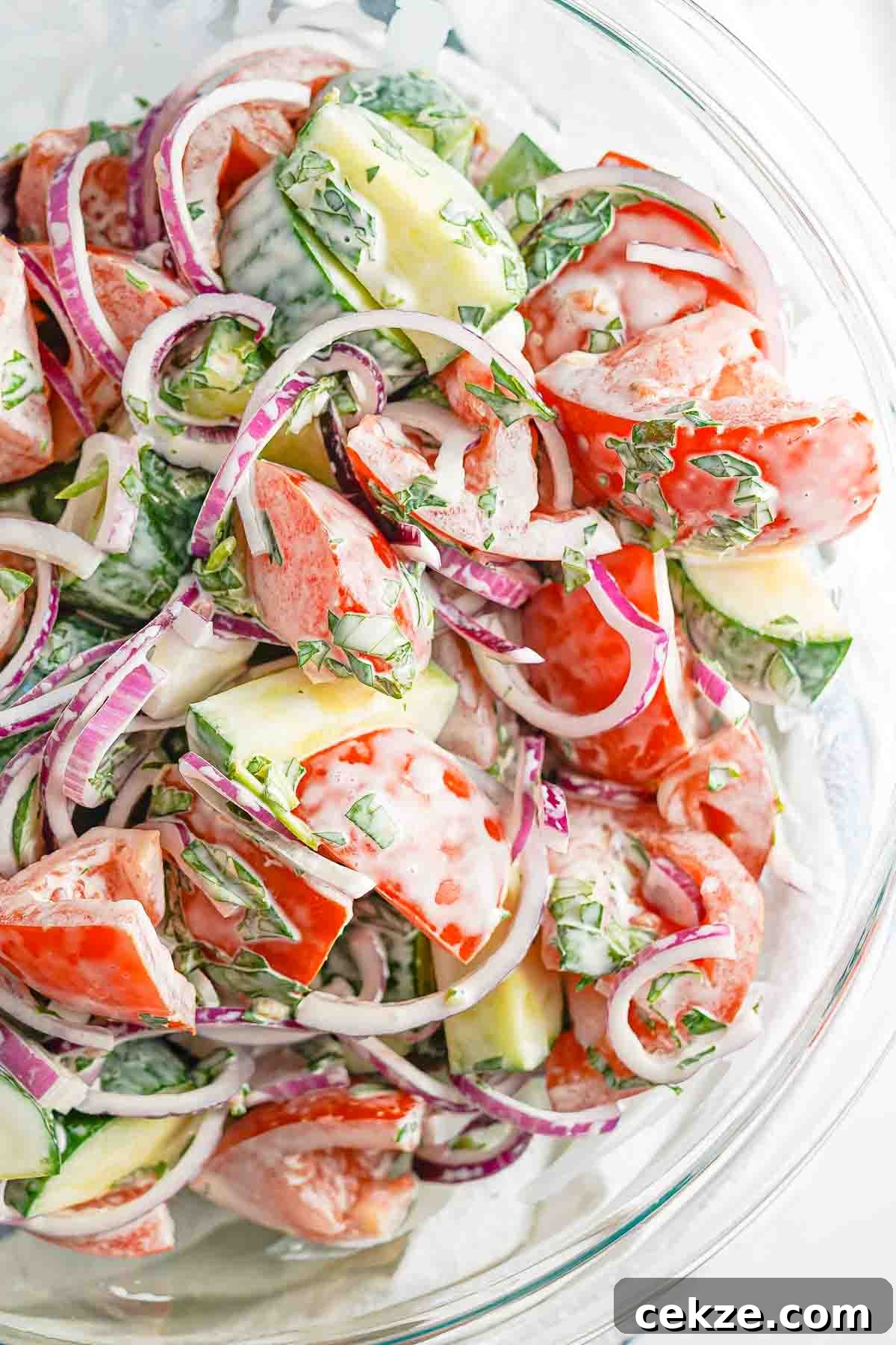creamy cucumber tomato salad with onions in glass bowl.