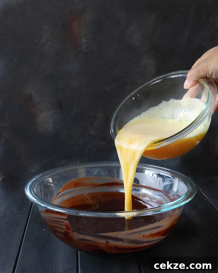 Pouring egg and sugar mixture into a glass mixing bowl filled with melted chocolate mixture