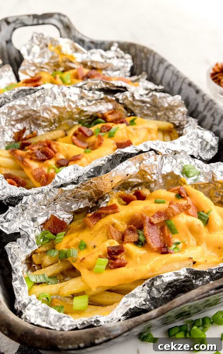 Loaded Dirty Fries Recipe: Crispy Fries Topped with Cheese & Bacon 11 close up shot of aluminum foils of Dirty Fries topped with cheese then garnished with bacon bits and green onions