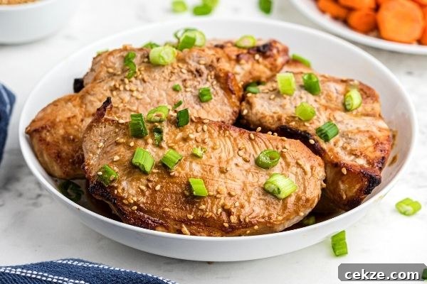 Juicy teriyaki pork chops served in a white bowl, with chopped green onions and sprinkles of sesame seeds on top.