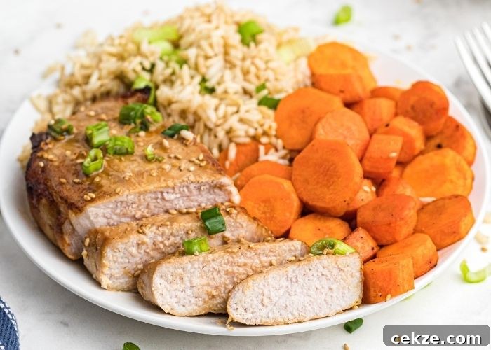Juicy pork chops cut into slices, served with carrots and rice on a white plate.