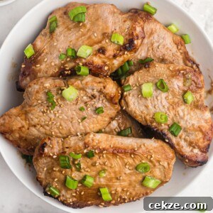 Juicy pork chops cooked and served in a white shallow bowl. Sprinkled with green onions and sesame seeds.